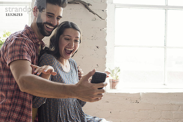 Verspieltes junges Paar mit einem Selfie im Loft