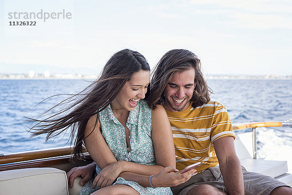 Glückliches Paar auf einer Bootsfahrt mit Blick aufs Handy