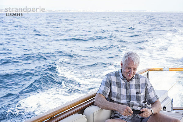 Senior auf einer Bootsfahrt mit Blick auf das Handy