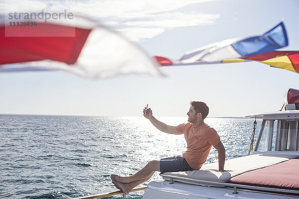Junger Mann  der auf einem Boot sitzt und einen Selfie nimmt.