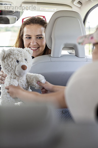 Mutter schaut sich die Tochter an  die mit dem Teddybär spielt und einen Roadtrip macht.