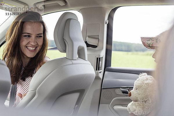 Mutter und Tochter auf Roadtrip sitzend im Auto mit Teddybär