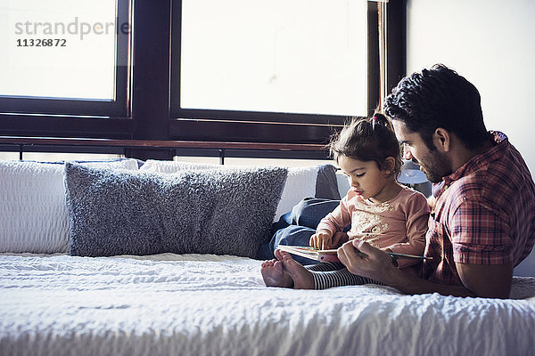 Vater und Tochter lesen Buch  liegend auf dem Bett
