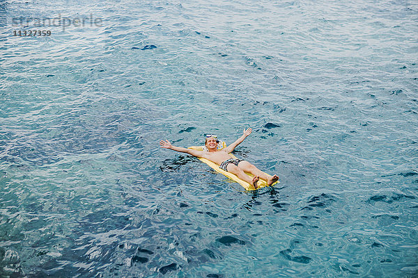 Fröhlicher junger Mann  der sich auf dem Luftbett im Meer entspannt.