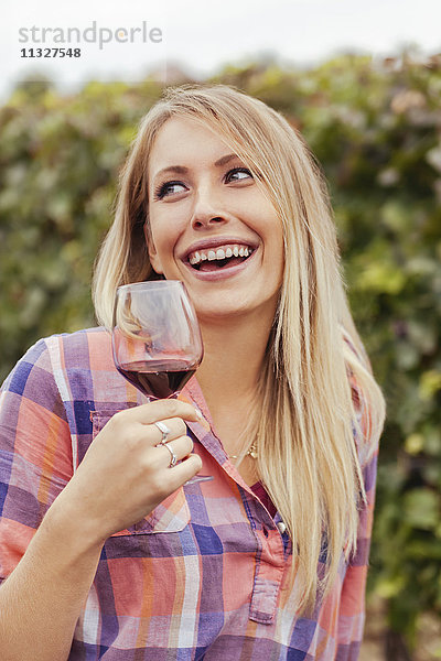 Glückliche junge Frau in einem Weinberg mit einem Glas Rotwein