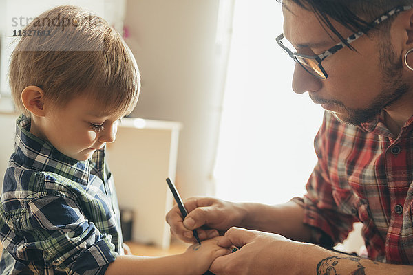 Vater malt Tattoo auf die Hand des Sohnes