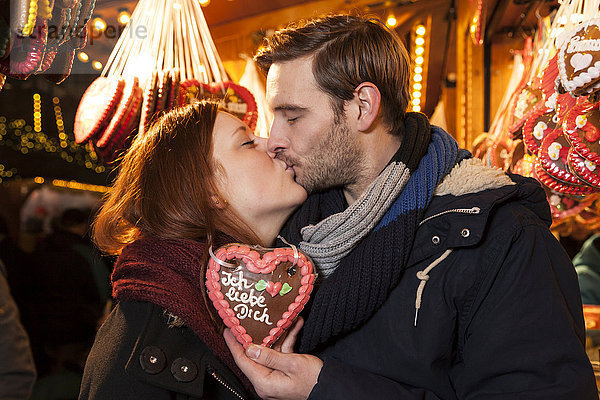 Paar küsst sich auf Weihnachtsmarkt mit deutschem Lebkuchenherz