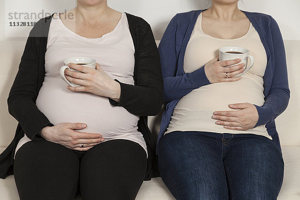 zwei schwangere Frauen auf dem Sofa sitzend mit Kaffee