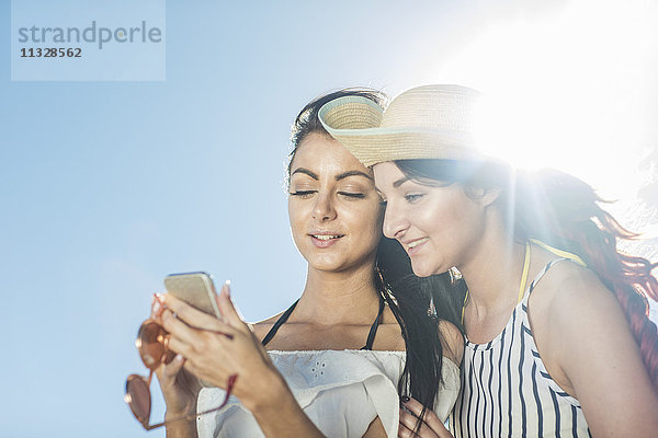 Zwei junge Frauen mit Handy unter blauem Himmel