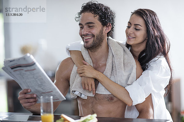 Lächelndes junges Paar zu Hause beim Zeitungslesen