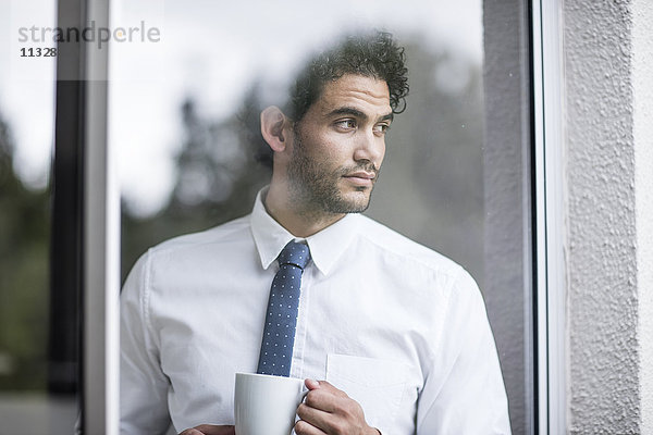 Geschäftsmann mit Tasse Kaffee aus dem Fenster schauend