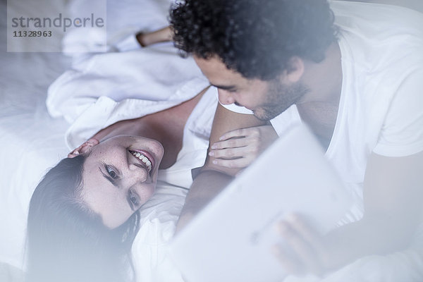 Lächelndes junges Paar im Bett mit Tablette
