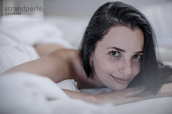 Porträt einer lächelnden jungen Frau im Bett liegend