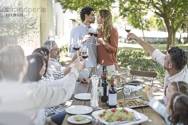 Pärchenküssen beim Mittagessen im Garten mit Rotwein