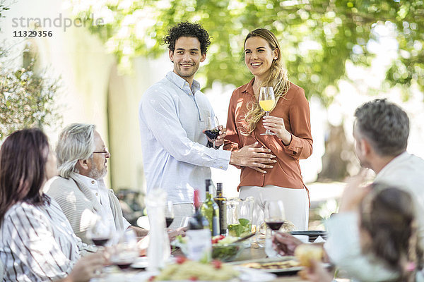 Ein junges Paar  das einen Toast ausspricht  mit der Ankündigung einer Schwangerschaft für die Familie während des Mittagessens außerhalb der Familie.