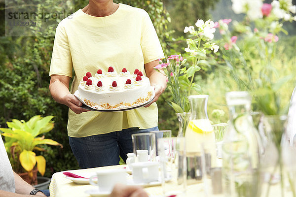 Reife Frau serviert Sahnetorte im Garten