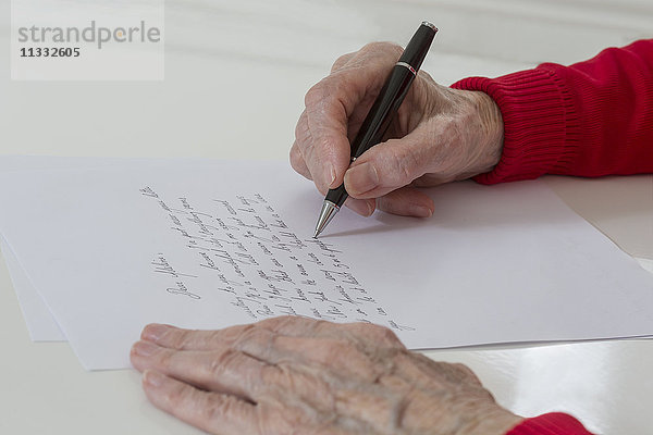Ältere Frau schreibt auf ein weißes Blatt.