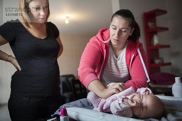 Reportage über eine freiberufliche Hebamme bei Hausbesuchen nach der Entbindung. Die Hebamme zeigt einer frischgebackenen Mutter  wie sie den Bauch ihres Babys massiert.