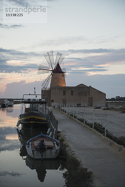 Boote im Kanal mit traditioneller Windmühle gegen den Himmel bei Sonnenuntergang festgemacht