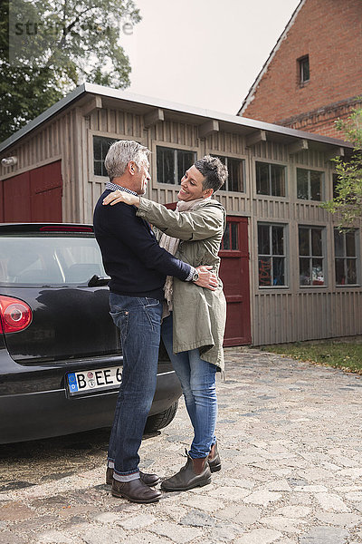 Glückliches Paar umarmt mit dem Auto gegen Haus