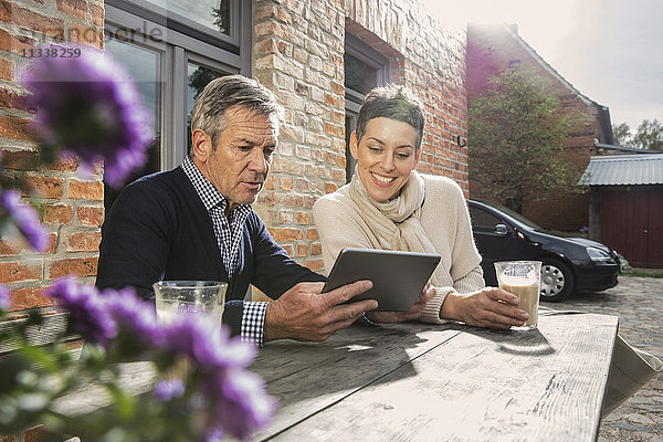 Erwachsenes Paar sitzend mit digitalem Tablett und Kaffee im Hinterhof