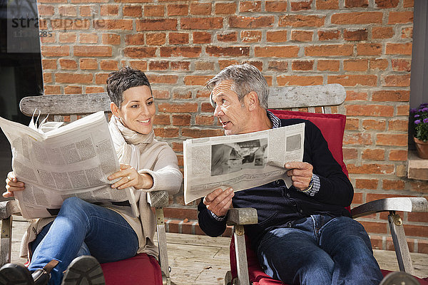 Mann zeigt Zeitung der glücklichen Frau  während er im Hinterhof sitzt