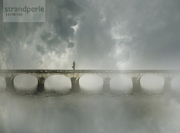 Geschäftsmann steht allein auf einer Brücke im Nebel