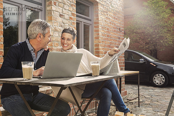 Fröhliches reifes Paar liest Zeitung mit Laptop im Hinterhof