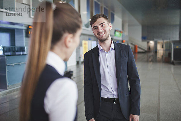 Junger Geschäftsmann lächelt beim Anblick der Geschäftsfrau am Flughafen