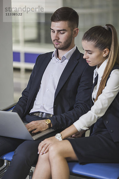 Junge Geschäftsfrau sitzend von Geschäftsmann mit Laptop am Flughafen