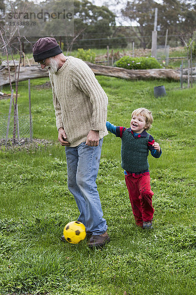 Volle Länge von Großvater und Enkel beim Fußballspielen auf der Wiese