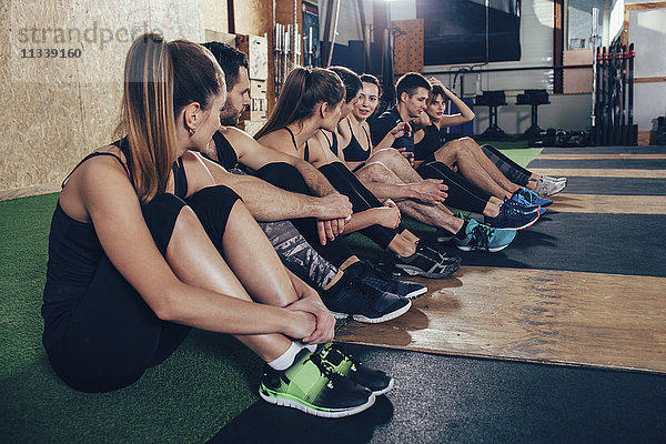 Sportlerinnen und Sportler beim Sitzen auf dem Teppich im Fitnessstudio