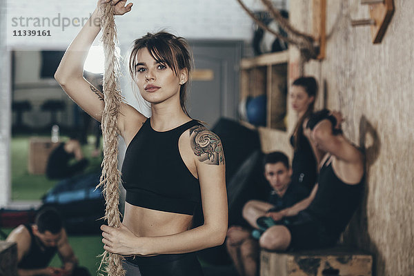 Porträt einer selbstbewussten Sportlerin  die im Fitnessstudio mit Freunden im Hintergrund steht.