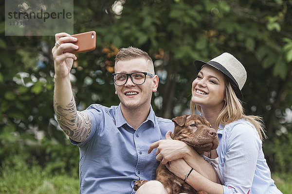 Ein Paar mit ihrem Shar-pei/Staffordshire Terrier im Park mit einem Selfie.