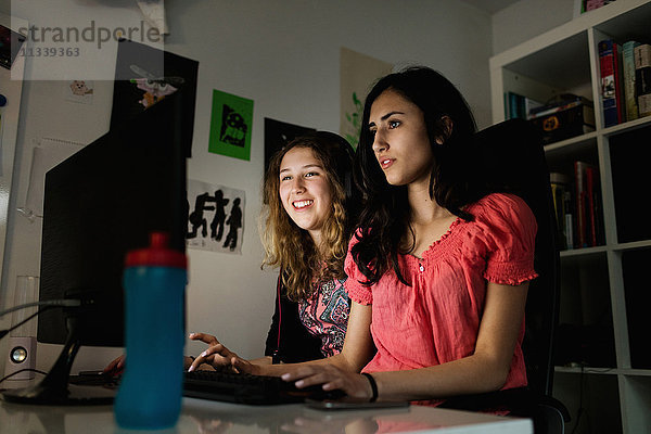 Fröhliches Teenagermädchen mit Computer und Freund in der Dunkelkammer zu Hause