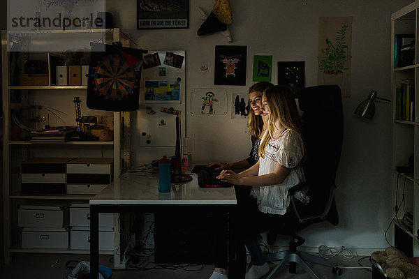 Teenager-Mädchen mit Computer am Tisch in der Dunkelkammer zu Hause