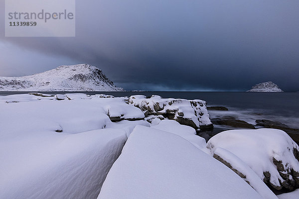 Sturmwolken auf den schneebedeckten Gipfeln spiegeln sich nachts im kalten Meer  Haukland  Lofoten  Nordnorwegen  Skandinavien  Europa