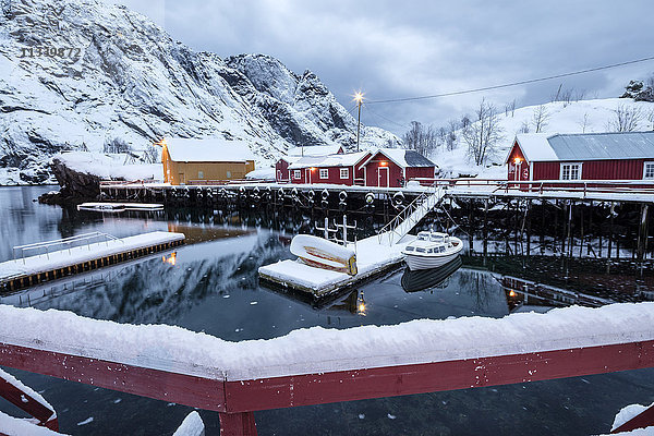 Kaltes Meer und schneebedeckte Gipfel umrahmen das Fischerdorf in der Abenddämmerung  Nusfjord  Nordland  Lofoten  Nordnorwegen  Skandinavien  Europa