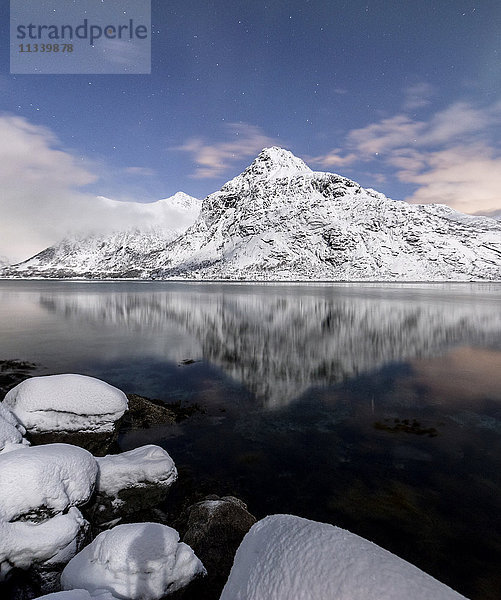 Die schneebedeckten Gipfel spiegeln sich im kalten Meer unter einem Sternenhimmel  Vareid  Flakstad  Nordland  Lofoten  Nordnorwegen  Skandinavien  Europa