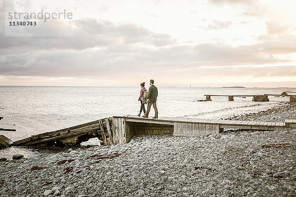 Paar  das bei Sonnenuntergang auf dem Steg am Strand gegen den Himmel läuft.