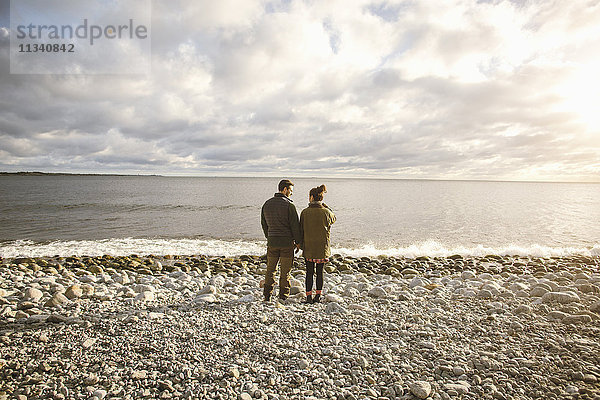 Rückansicht des Paares  das am felsigen Ufer am Strand gegen den Himmel steht.