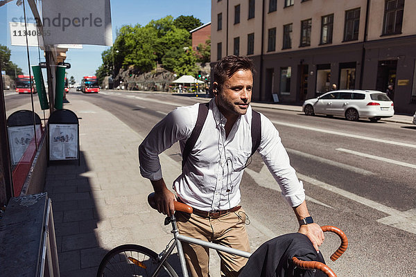 Nachdenklicher Geschäftsmann steht mit dem Fahrrad auf dem Bürgersteig in der Stadt.