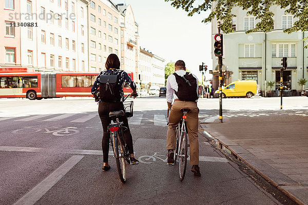 Rückansicht von Geschäftsleuten  die auf der Stadtstraße Fahrrad fahren