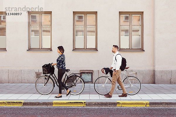 Seitenansicht von Geschäftskollegen  die mit Fahrrädern auf dem Bürgersteig laufen