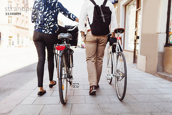Niederquerschnitt Rückansicht von Geschäftskollegen  die mit Fahrrädern auf dem Bürgersteig gehen