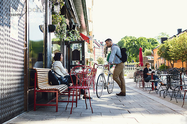 Volle Länge des Geschäftsmannes mit Fahrrad im Gespräch mit Kollegen im Straßencafé