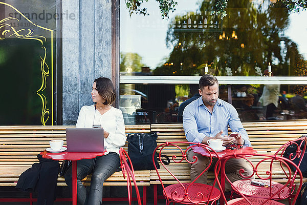 Geschäftsleute  die Technologien im Straßencafé nutzen.