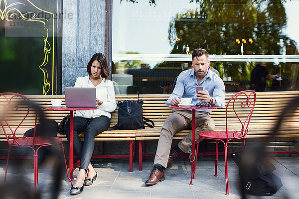 Geschäftsleute mit Laptop und Smartphone im Straßencafé