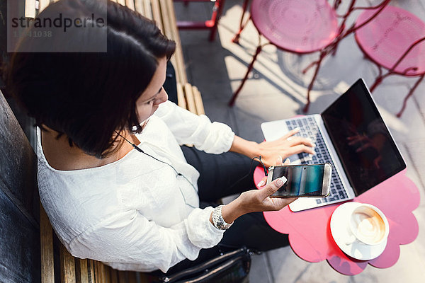 Hochwinkelansicht der Geschäftsfrau mit Smartphone und Laptop im Bürgersteigcafe