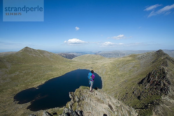 Eine Frau steht auf dem Gipfel des Striding Edge mit Blick auf den Red Tarn und den Ullswater in der Ferne  Lake District National Park  Cumbria  England  Vereinigtes Königreich  Europa